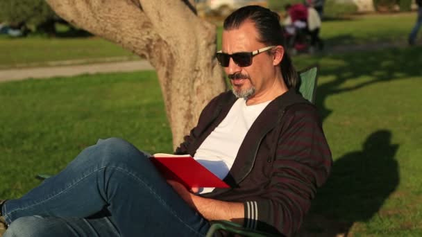 Man die een boek leest in het park — Stockvideo