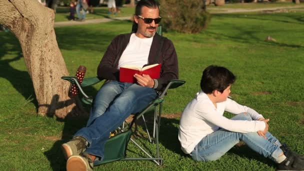 Father reading to son in the park on a sunny day — Stock Video