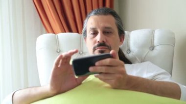 Sıkılmış, adam akıllı telefon kullanarak kanepede
