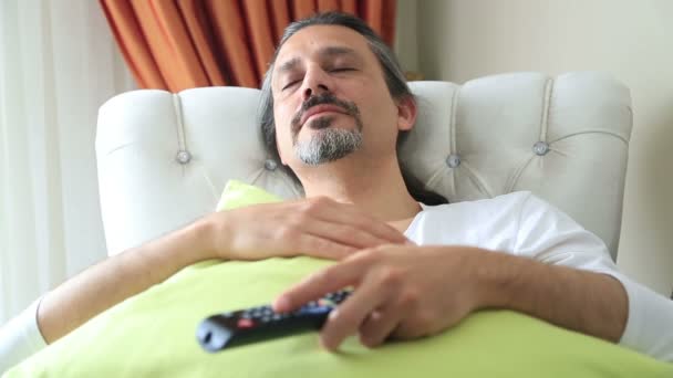 Yawning middle age man on couch with TV remote control — Stock Video