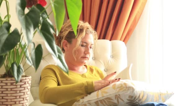 Vrouw op de Bank een boek lezen en lachend naar een camera — Stockvideo