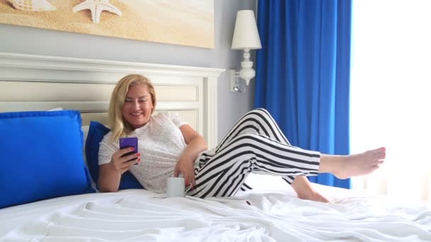 Blonde vrouw liggend op een bed en het gebruik van slimme telefoon — Stockvideo