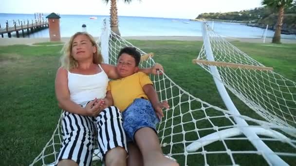 Μητέρα και γιος χαλαρώνοντας σε μια αιώρα δίπλα στη θάλασσα — Αρχείο Βίντεο