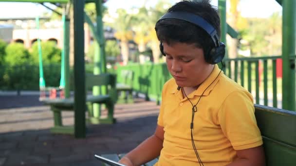 与耳机使用数字平板电脑在公园里的小男孩 — 图库视频影像