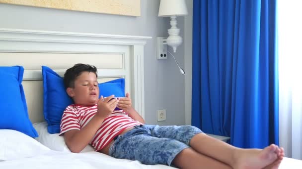 Niño acostado en una cama y usando un teléfono inteligente — Vídeo de stock