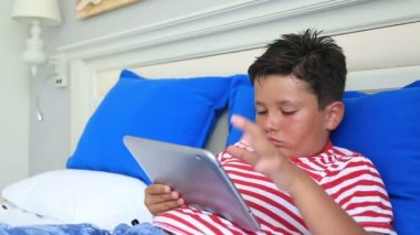 Bir yatakta yatarken ve dijital tablet bilgisayar kullanarak çocuk