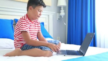 Bir yatakta yatarken ve dizüstü bilgisayar kullanan çocuk