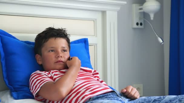 Niño acostado en una cama y hablando en el teléfono móvil — Vídeo de stock