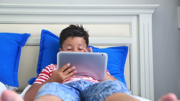 Ребенок лежит на кровати и использует цифровой планшетный компьютер — стоковое видео