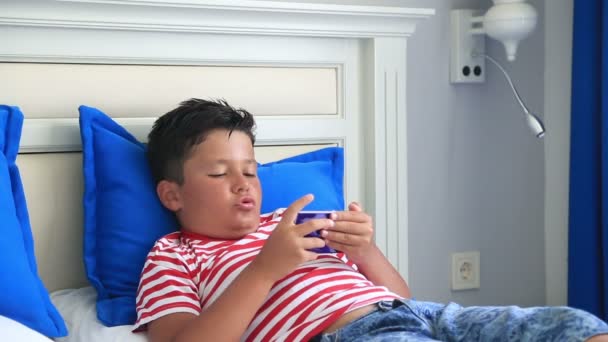 Niño acostado en una cama y usando un teléfono inteligente — Vídeos de Stock