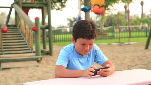 Kind entspannt mit Smartphone auf Spielplatz 2 — Stockvideo