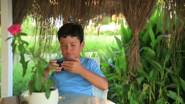 Παιδί χαλαρωτικό με smartphone στο καλοκαίρι καφέ — Αρχείο Βίντεο