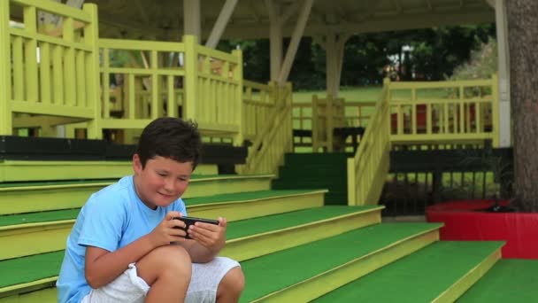 Child sitting on a stairs with smartphone — Stock Video