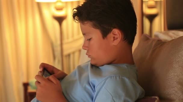 Πορτρέτο του ένα αστείο νεαρό αγόρι που παίζει στο smartphone στο σπίτι — Αρχείο Βίντεο