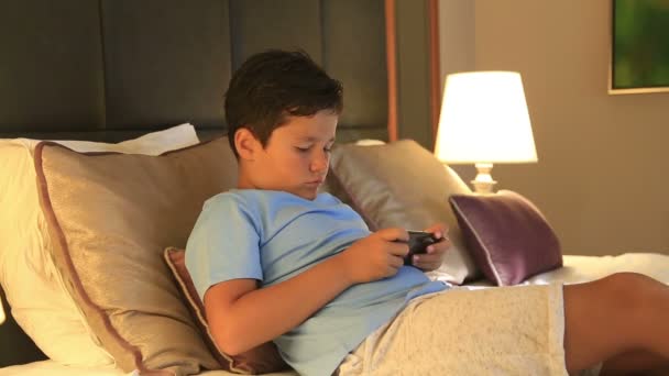 Портрет смішного хлопчика, який грає на смартфоні вдома — стокове відео