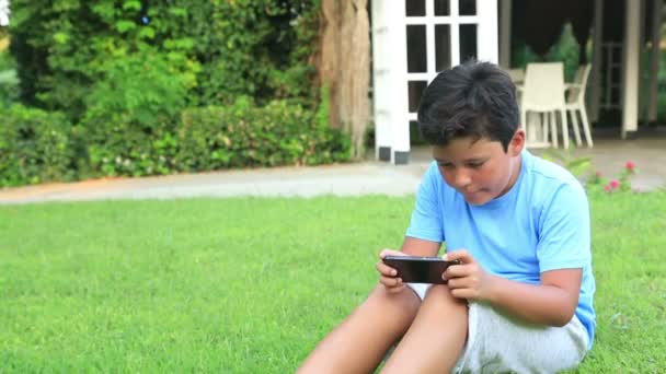 Мальчик играет в смартфон на траве — стоковое видео