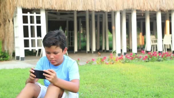 Joven jugar smartphone en la hierba — Vídeos de Stock