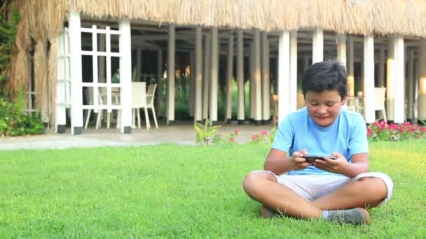 Jovem menino jogar smartphone na grama — Vídeo de Stock