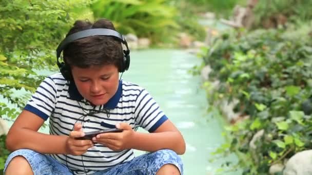 Niño con auriculares de juego en la naturaleza — Vídeo de stock