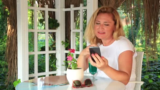 Wanita pirang dengan smartphone santai di kafe musim panas — Stok Video
