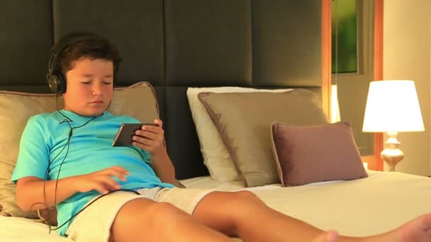 Kind met hoofdtelefoon liggend op een bed en luisteren naar muziek met Mp3-speler — Stockvideo