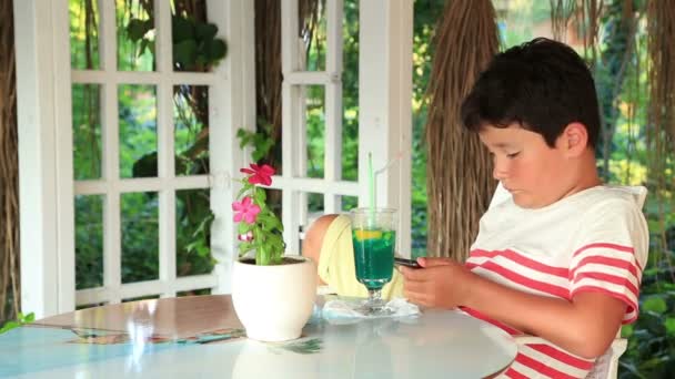 Милый ребенок с помощью смартфона в летнем кафе — стоковое видео