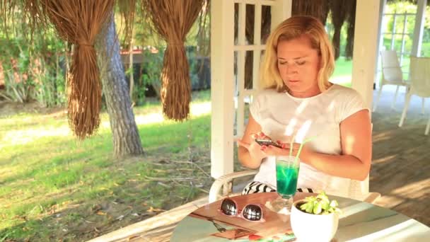 Женщина сидит в летнем кафе и пользуется смартфоном — стоковое видео