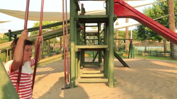 Niño feliz balanceo en el patio de recreo — Vídeo de stock