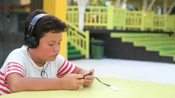 Niño pequeño con auriculares usando teléfono inteligente — Vídeos de Stock