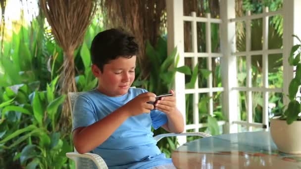 Niño relajante con teléfono inteligente en la cafetería de verano — Vídeos de Stock