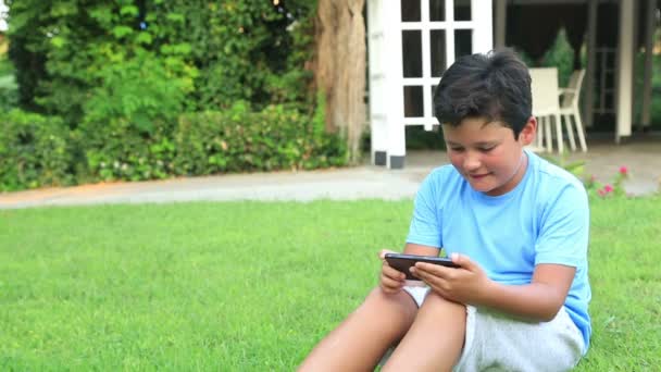 Jonge jongen spelen smartphone op het gras — Stockvideo