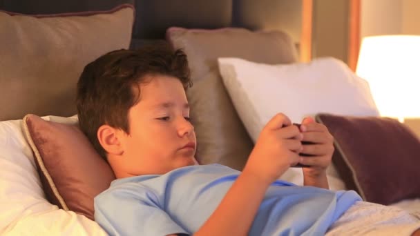 Unga burunette barn med smart telefon i sovrum — Stockvideo