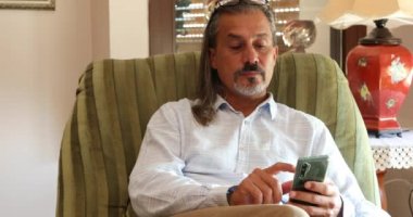 Kanepede oturan ve akıllı telefon kullanan orta yaşlı bir İspanyol 'un portresi.
