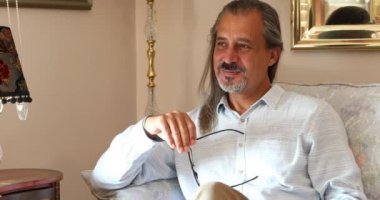 Mutlu orta yaşlı adam koltukta oturuyor ve kameraya gülümsüyor.