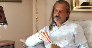 Düşünceli, orta yaşlı bir adamın portresi. Evdeki kanepede oturuyor.