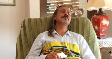 Hasta, yorgun bir adam kanepede battaniyeyle otururken üşütmüş.