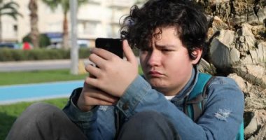 Dışarıda tek başına oturan yakışıklı bir gencin portresi. Çocuk ekranı seyrediyor, okuyor, daktilo ediyor, oyunlar oynuyor. Teknoloji, internet iletişimi ve insan konsepti, akıllı telefon bağımlılığı