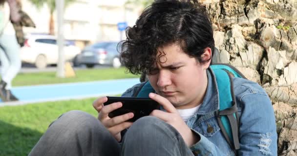 ハンサムな10代の少年の肖像画は 屋外だけで子供の画面を見て ゲームをプレイ座っている テクノロジー インターネット通信と人々の概念 スマートフォン中毒 — ストック動画