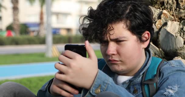 一个英俊的少年独自坐在户外看电影 玩游戏的画像 网络通信和人的概念 智能手机成瘾 — 图库视频影像