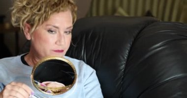 Çekici bir kadının portresi. Sarı saçlı. Aynaya bakıyor ve iç mekâna makyaj yapıyor.