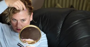 Çekici bir kadının portresi. Sarı saçlı. Aynaya bakıyor ve iç mekâna makyaj yapıyor.