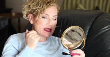 Çekici bir kadının portresi. Sarı saçlı. Aynaya bakıyor ve iç mekâna makyaj yapıyor.