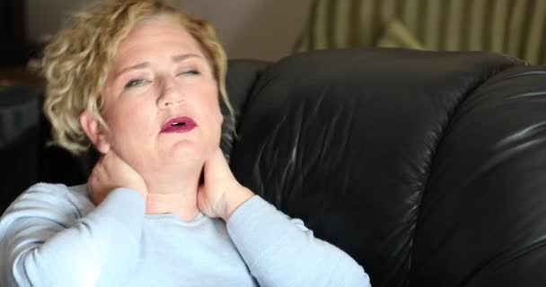 痛苦的女人坐在家里的沙发上按摩着脖子和肩膀 — 图库视频影像