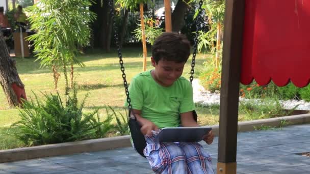 Niño balanceándose y usando tableta digital — Vídeo de stock