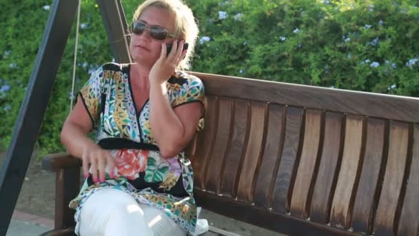 Frau sitzt auf Gartenschaukel und nutzt Smartphone — Stockvideo