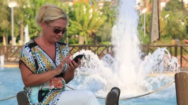 Frau benutzt Smartphone in der Nähe des Parkbrunnens — Stockvideo