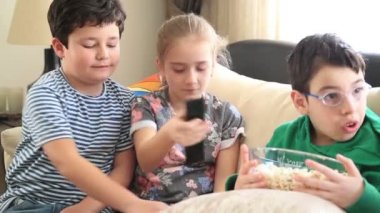 Çocuklar televizyon izliyor ve patlamış mısır yiyor.