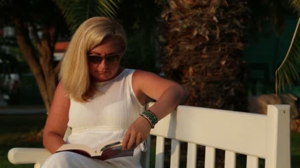 Een vrouw die een boek leest in het park — Stockvideo