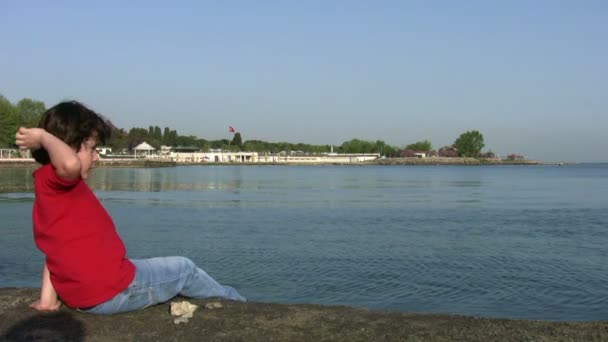 Pequeño niño lanzando piedras al mar — Vídeos de Stock