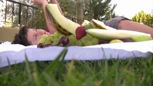 Mały chłopiec jedząc owoce na piknik na świeżym powietrzu — Wideo stockowe